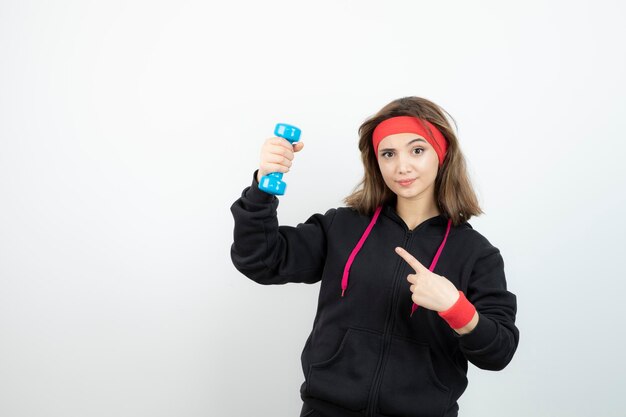 Mujer deportiva joven de pie y apuntando a la mancuerna azul. foto de alta calidad