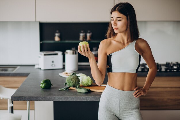 Mujer deportiva con manzana en la cocina