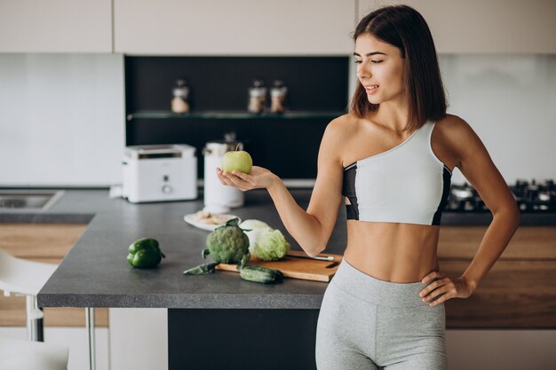 Mujer deportiva con manzana en la cocina