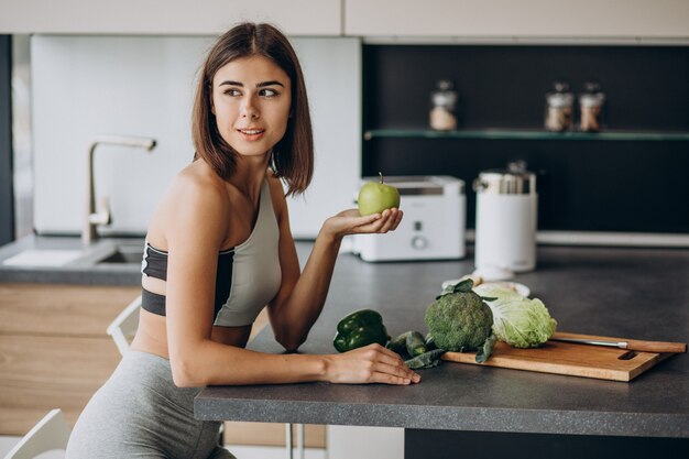 Mujer deportiva con manzana en la cocina