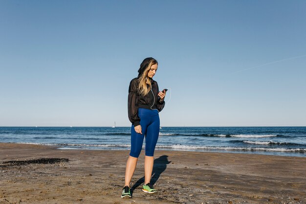 Mujer deportiva mirando a smartphone en la playa