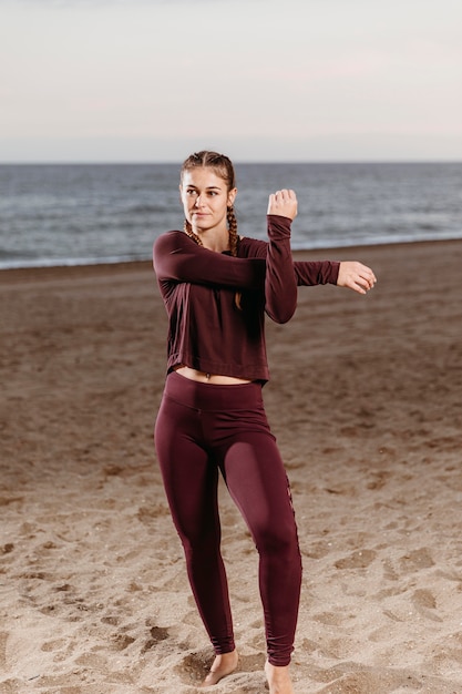 Foto gratuita mujer deportiva por la playa estirando