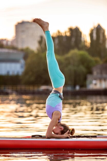 Mujer deportiva en posición de yoga en paddleboard, haciendo yoga en sup board, ejercicio para flexibilidad y estiramiento de músculos. Mujer practicando yoga en la tabla de paddle por la mañana