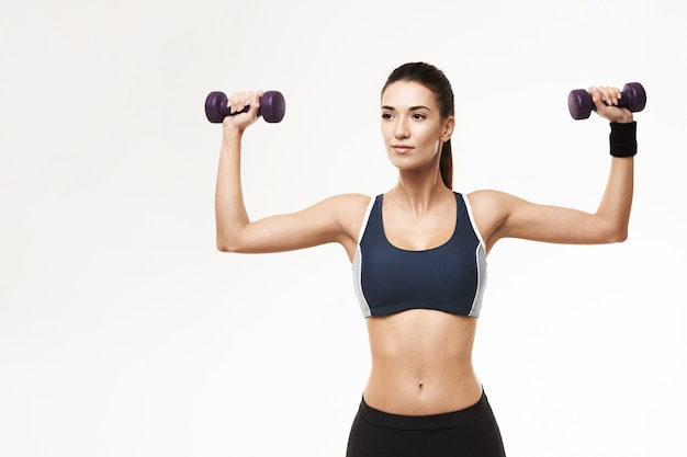 La mujer deportiva en ropa deportiva que entrena arma con pesas de gimnasia en blanco.