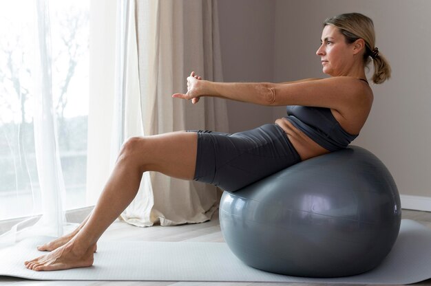 Mujer deportiva en ropa de fitness azul sentado junto a una pelota de fitness