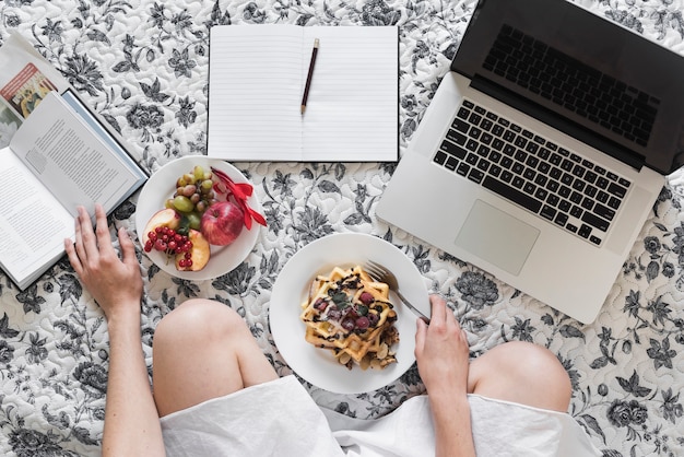 Mujer desayunando saludable mientras estudia en la cama