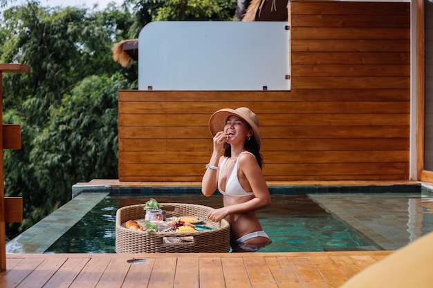 Mujer desayunando tropical saludable en villa en mesa flotante