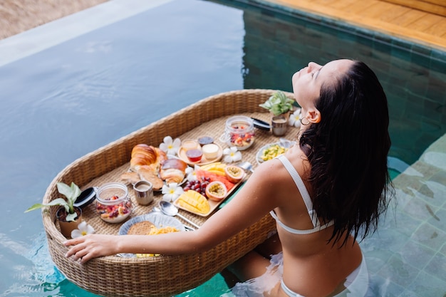 Mujer desayunando tropical saludable en villa en mesa flotante