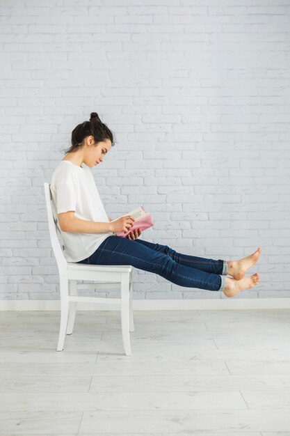 Mujer descalza disfrutando leyendo en la silla