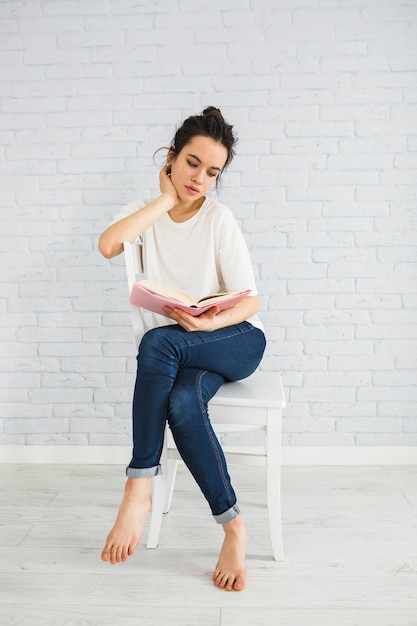 Mujer descalza leyendo buen libro en la silla