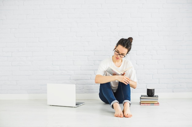 Mujer descalza leyendo cerca de la computadora portátil