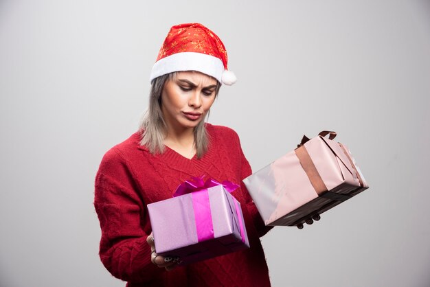 Mujer desconcertada con sombrero de Santa mirando los regalos de Navidad.