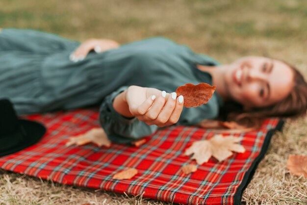 Mujer desenfocada sosteniendo hojas sobre una manta para picnic