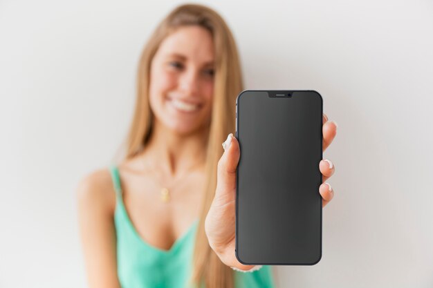 Mujer desenfocada de vista frontal mostrando su teléfono inteligente con pantalla vacía