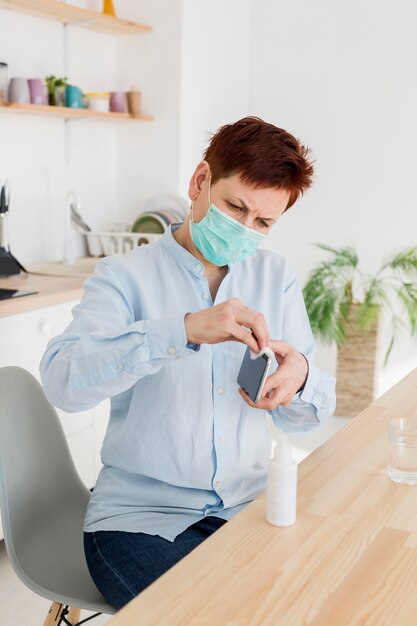 Mujer desinfectando su teléfono inteligente en casa