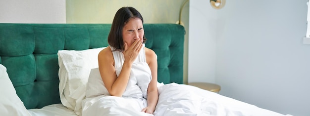 Foto gratuita mujer despertándose en la cama bostezando y haciendo muecas temprano en la mañana después de dormir sentada en el dormitorio