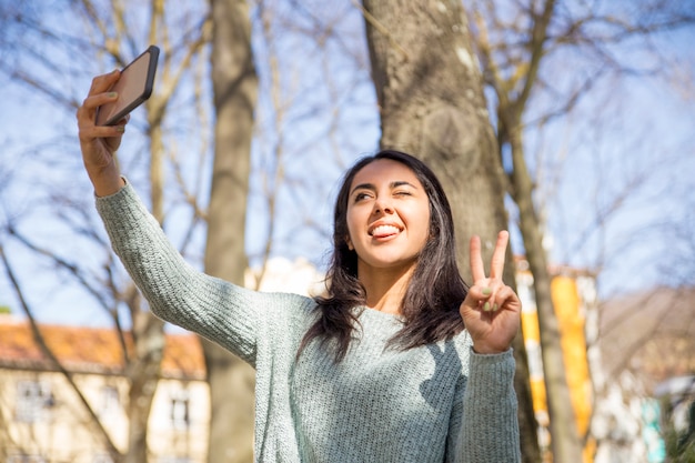 Mujer despreocupada haciendo muecas y tomando fotos selfie al aire libre