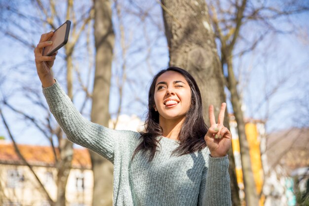 Mujer despreocupada haciendo muecas y tomando fotos selfie al aire libre