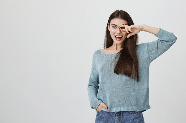 Mujer despreocupada mostrando bien firmar sobre ojo y sonriendo