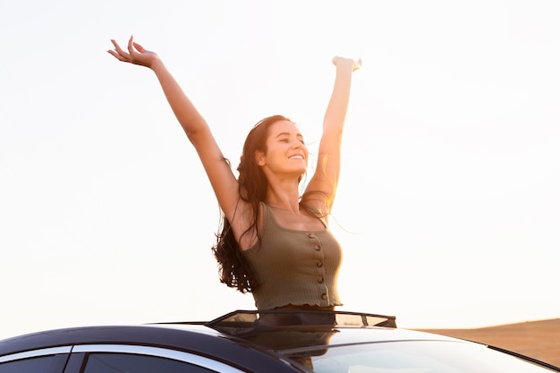 Mujer despreocupada posando desde su coche en la puesta de sol