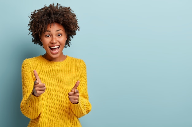 Mujer despreocupada saliente con un afro posando en un suéter rosa