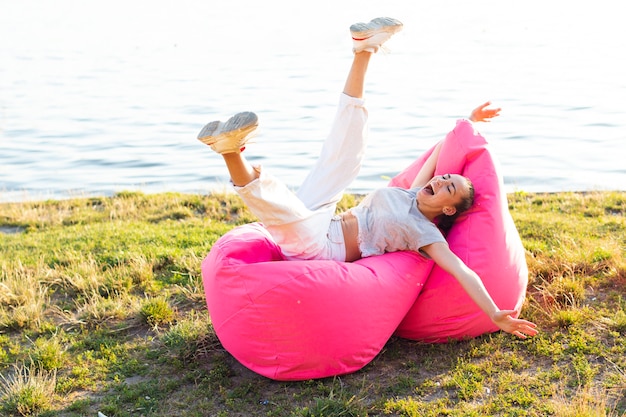 Mujer despreocupada de tiro largo que presenta en un beanbag rosado