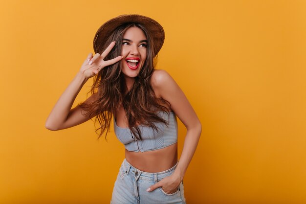 Mujer dichosa con maquillaje de moda posando con el signo de la paz y riendo