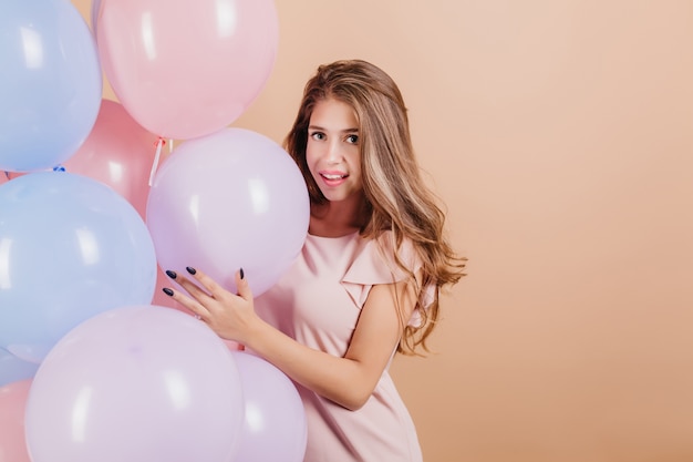 Mujer dichosa con pelo largo ondulado posando con globos de helio de colores