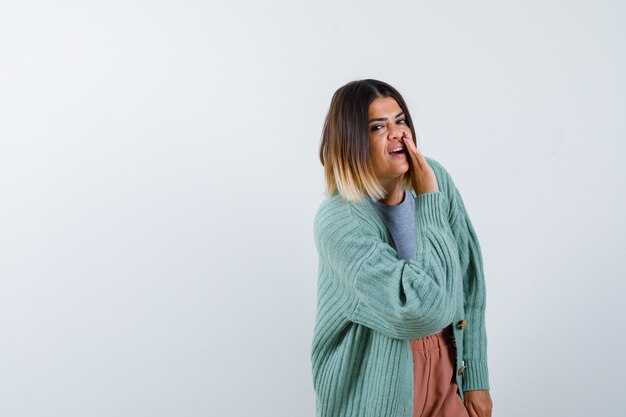 Mujer diciendo secretos detrás de la mano en ropa casual y mirando curiosa, vista frontal.