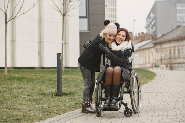 Mujer discapacitada en silla de ruedas con hija. Familia caminando afuera en el parque.