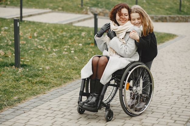 Mujer discapacitada en silla de ruedas con hija. Familia caminando afuera en el parque.