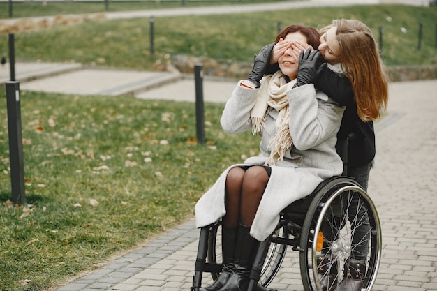 Mujer discapacitada en silla de ruedas con hija. Familia caminando afuera en el parque.