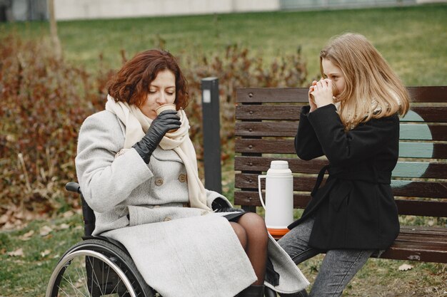 Mujer discapacitada en silla de ruedas con hija. Familia caminando afuera en el parque.