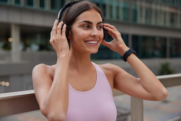 Mujer disfruta de salidas deportivas en auriculares inalámbricos para escuchar música durante el entrenamiento viste camiseta plantea al aire libre en borrosa