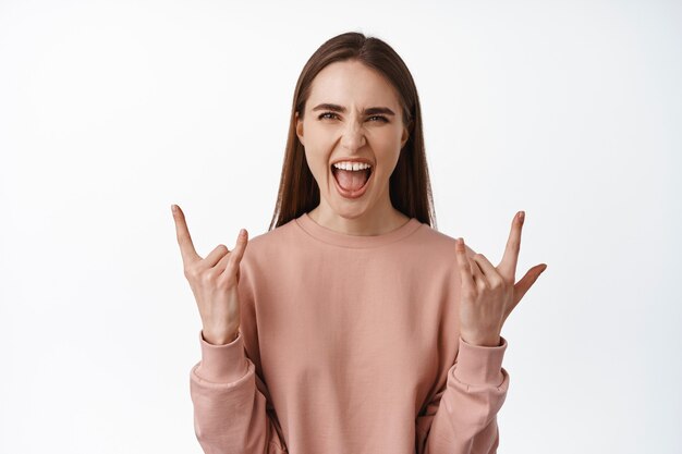 Mujer disfrutando de eventos, conciertos y fiestas, gritando de alegría y emoción, sacudiendo rock con cuernos de heavy metal, divirtiéndose en blanco