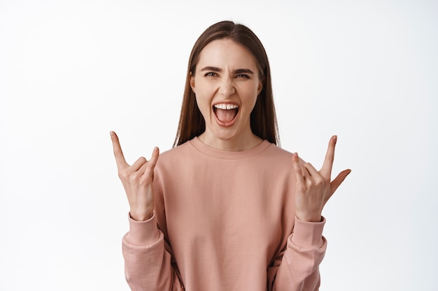 Mujer disfrutando de eventos, conciertos y fiestas, gritando de alegría y emoción, sacudiendo rock con cuernos de heavy metal, divirtiéndose en blanco