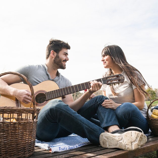 Mujer disfrutando de música en la guitarra tocada por su novio en un picnic