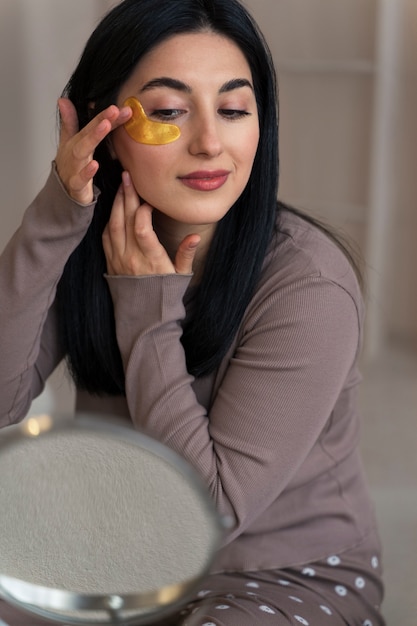 Foto gratuita mujer disfrutando de su rutina de belleza con parches dorados en los ojos