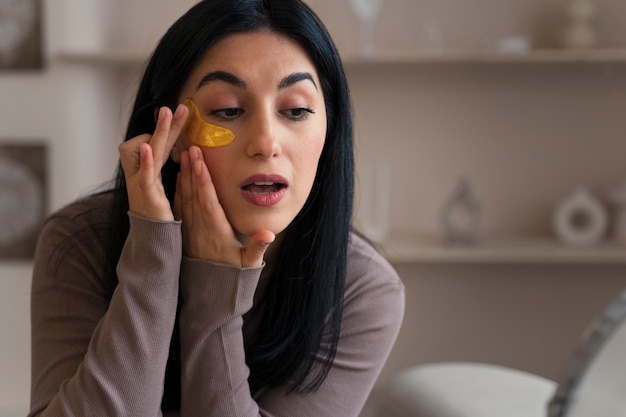 Foto gratuita mujer disfrutando de su rutina de belleza con parches dorados en los ojos