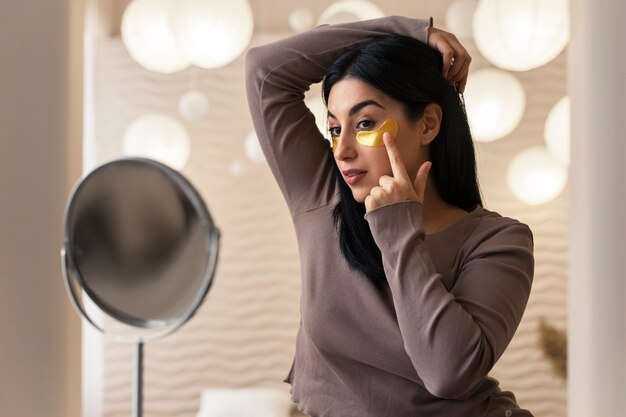 Mujer disfrutando de su rutina de belleza con parches dorados en los ojos