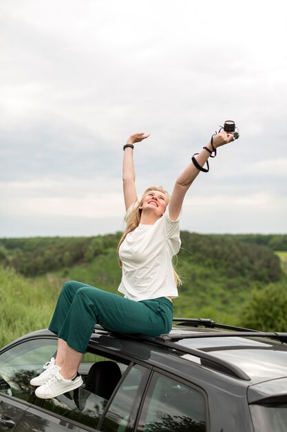 Mujer disfrutando de la vida mientras posa encima del coche