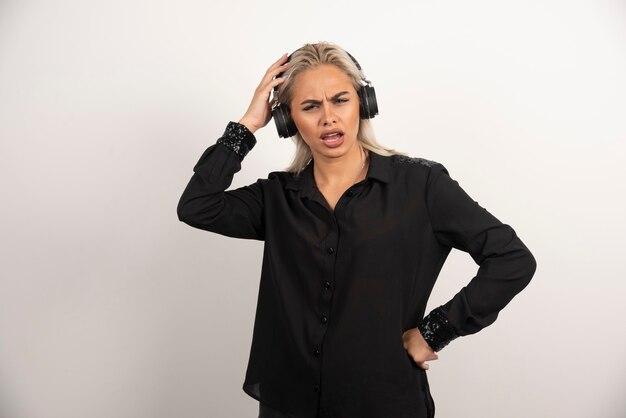Mujer disgustada con auriculares de pie sobre fondo blanco. Foto de alta calidad