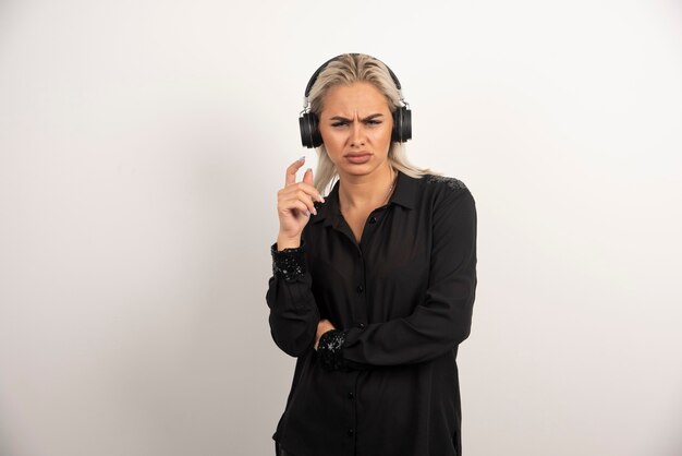 Mujer disgustada con auriculares de pie sobre fondo blanco. Foto de alta calidad