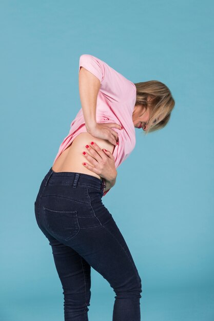 Mujer disgustada que sufre de dolor de espalda baja sobre fondo azul