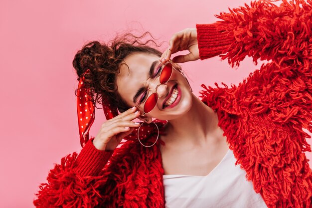 Mujer divertida en chaqueta mullida roja riendo sobre fondo rosa