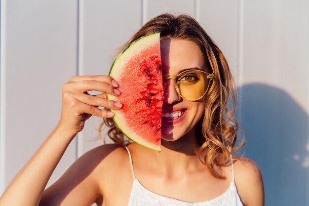 Mujer divertida en gafas de sol escondiendo la mitad de su cara con un pedazo de sandía