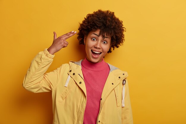 La mujer divertida sonriente alegre señala con el dedo a la sien como si se estuviera suicidando, explota el cerebro, inclina la cabeza, hace tonterías, tiene humor juguetón