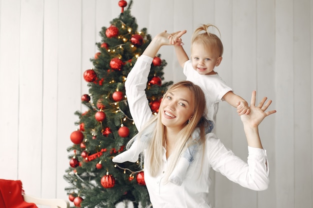 La mujer se divierte preparándose para la Navidad. Madre con camisa blanca está jugando con su hija. La familia está descansando en una sala festiva.