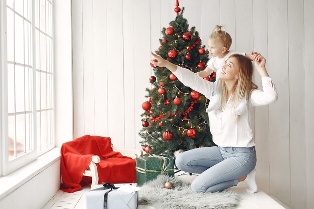 La mujer se divierte preparándose para la Navidad. Madre con camisa blanca está jugando con su hija. La familia está descansando en una sala festiva.
