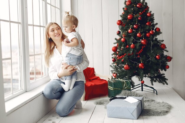 La mujer se divierte preparándose para la Navidad. Madre con camisa blanca está jugando con su hija. La familia está descansando en una sala festiva.